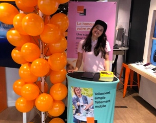 Animatrice accueillant les visiteurs à un stand événementiel décoré de ballons.