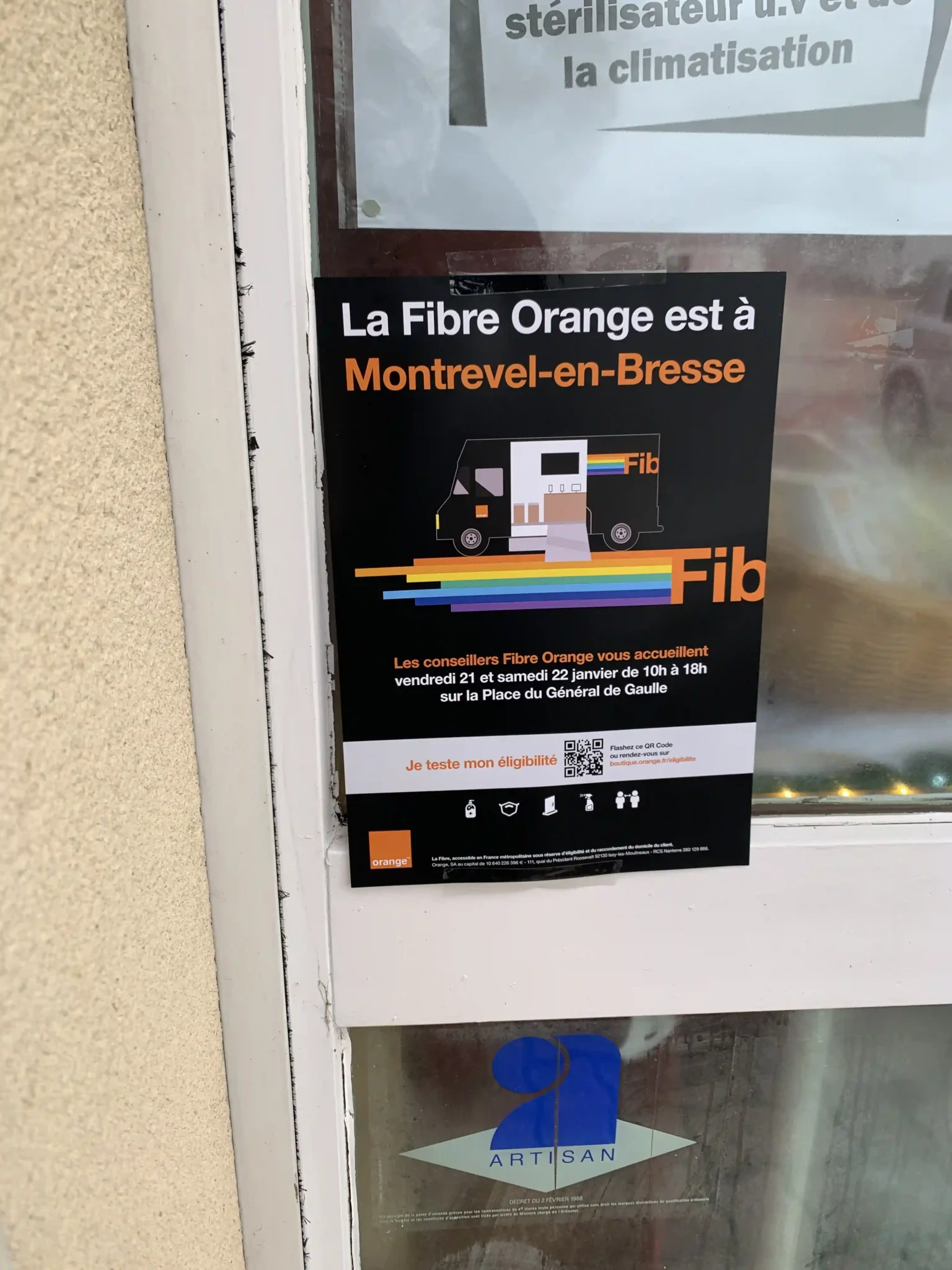 Affiche publicitaire « La Fibre Orange est à Montrevel-en-Bresse » collée sur une vitre de porte d’entrée de commerce.