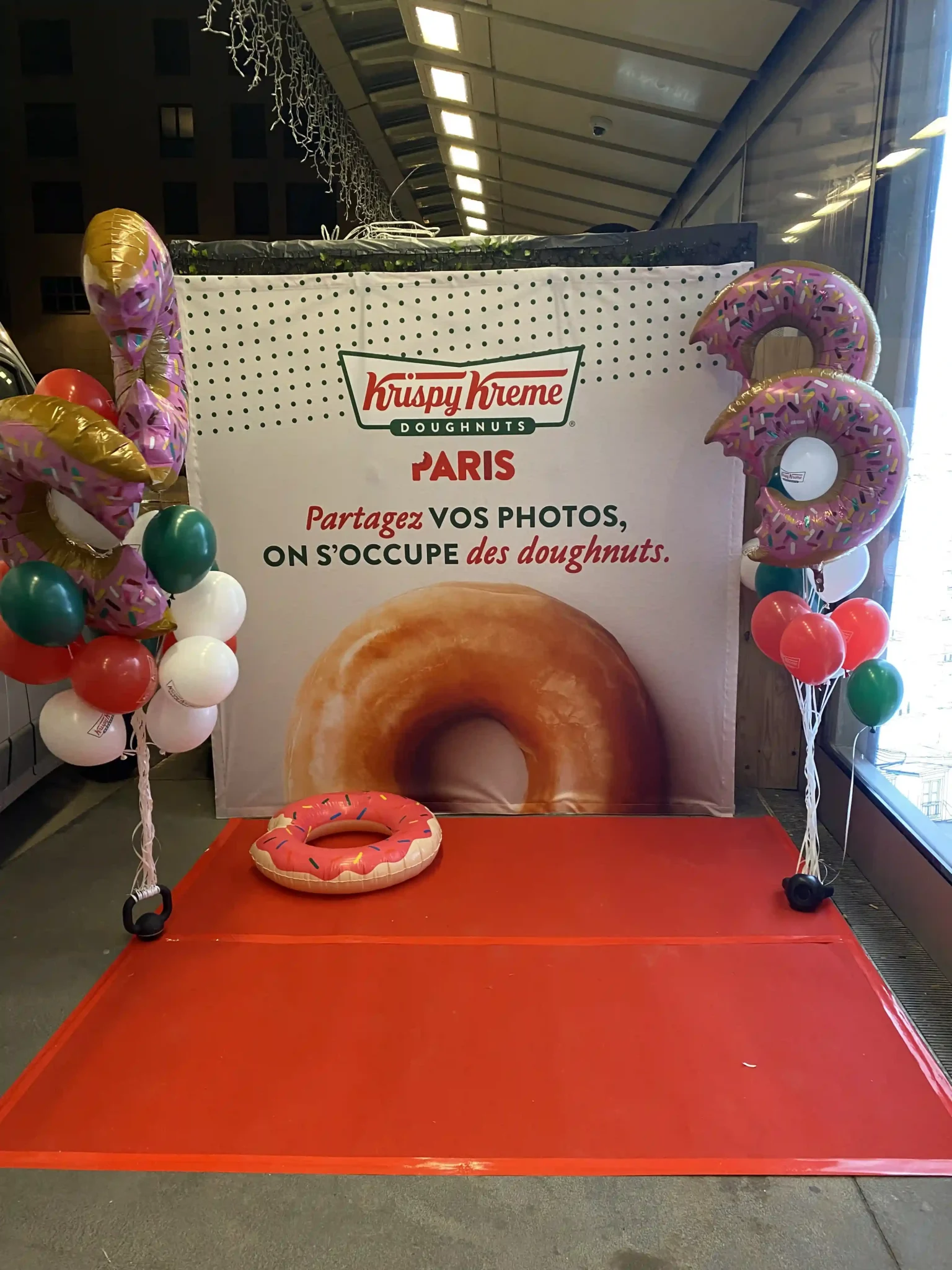 Décor événementiel personnalisé avec tapis rouge, ballons et fond photo pour une marque de donuts.