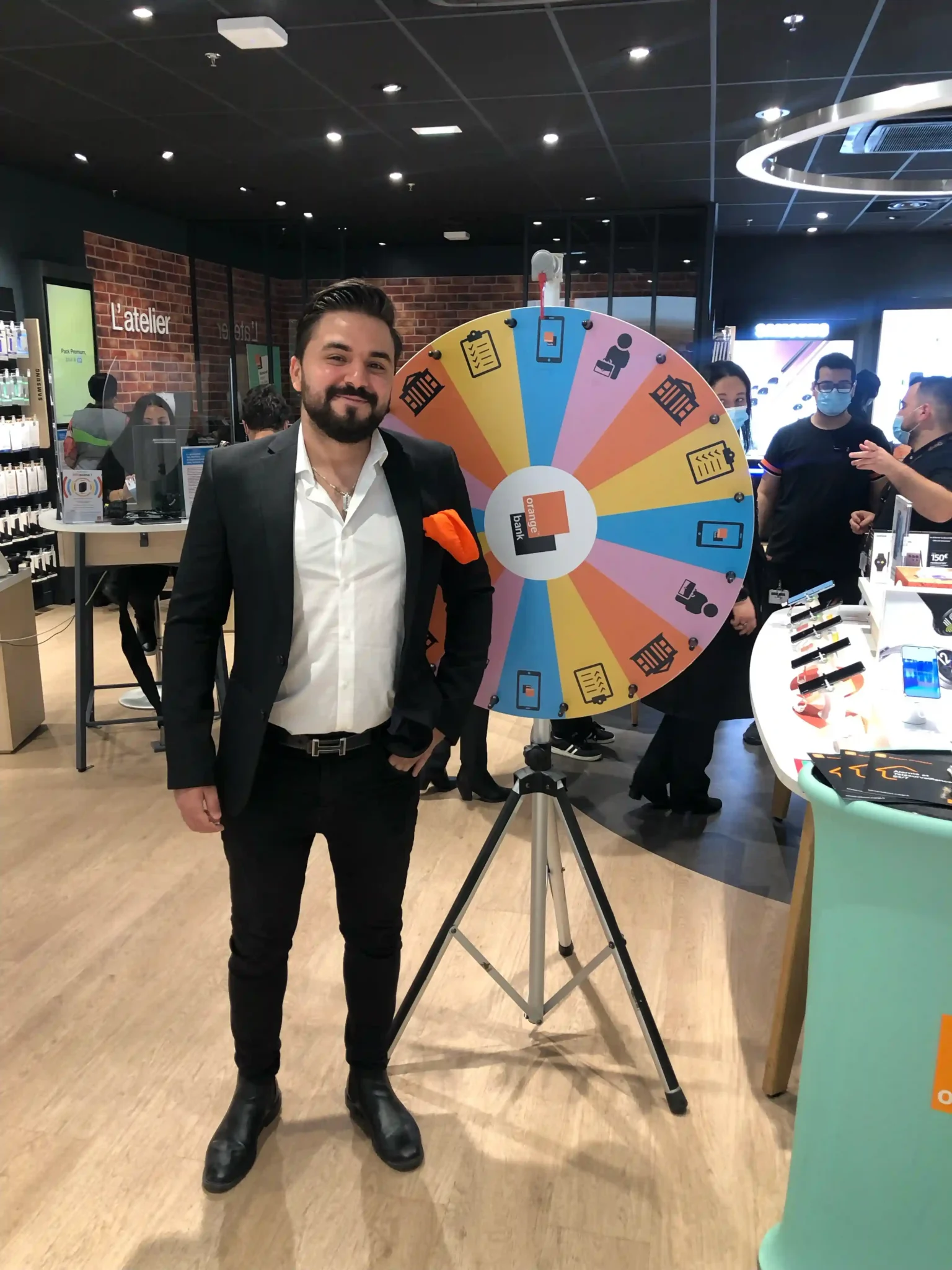 Un animateur en costume souriant devant une roue de la chance lors d’un événement promotionnel en magasin.