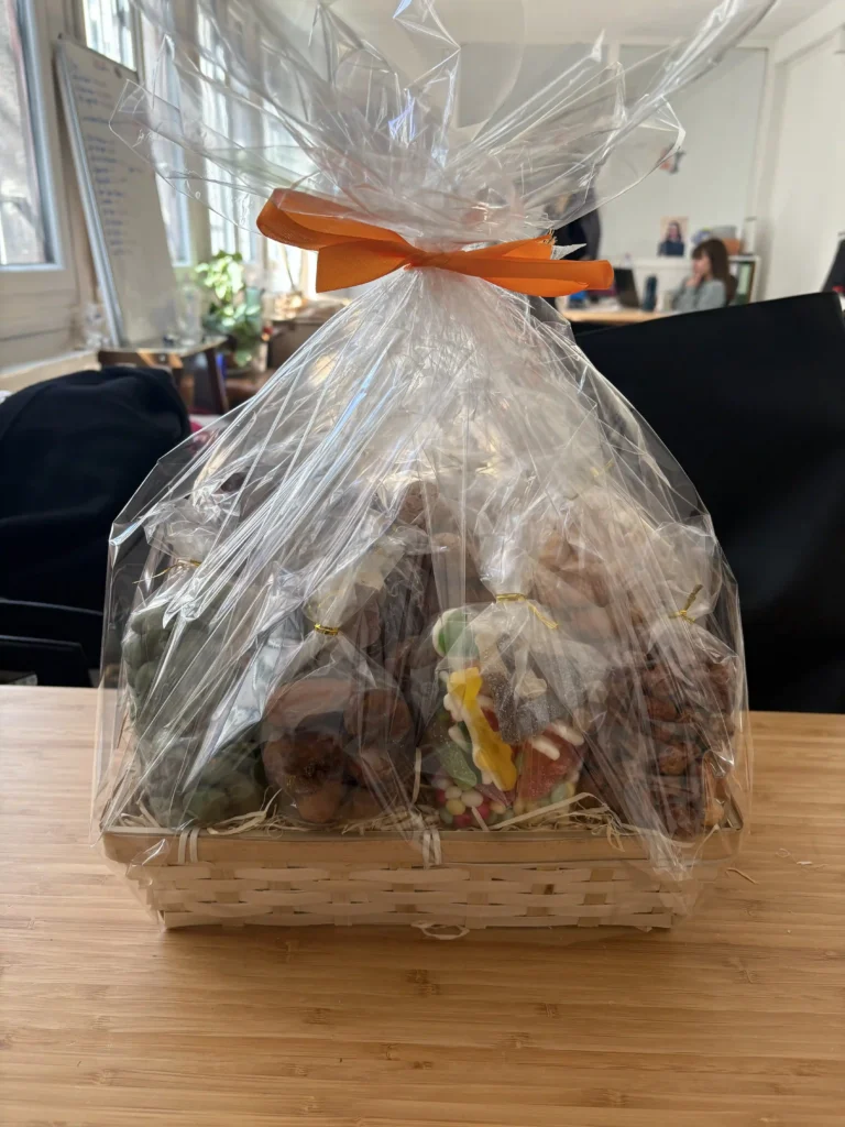 Un panier garni composé de plusieurs sachets de produits, soigneusement emballé dans du film transparent et fermé par un ruban orange.