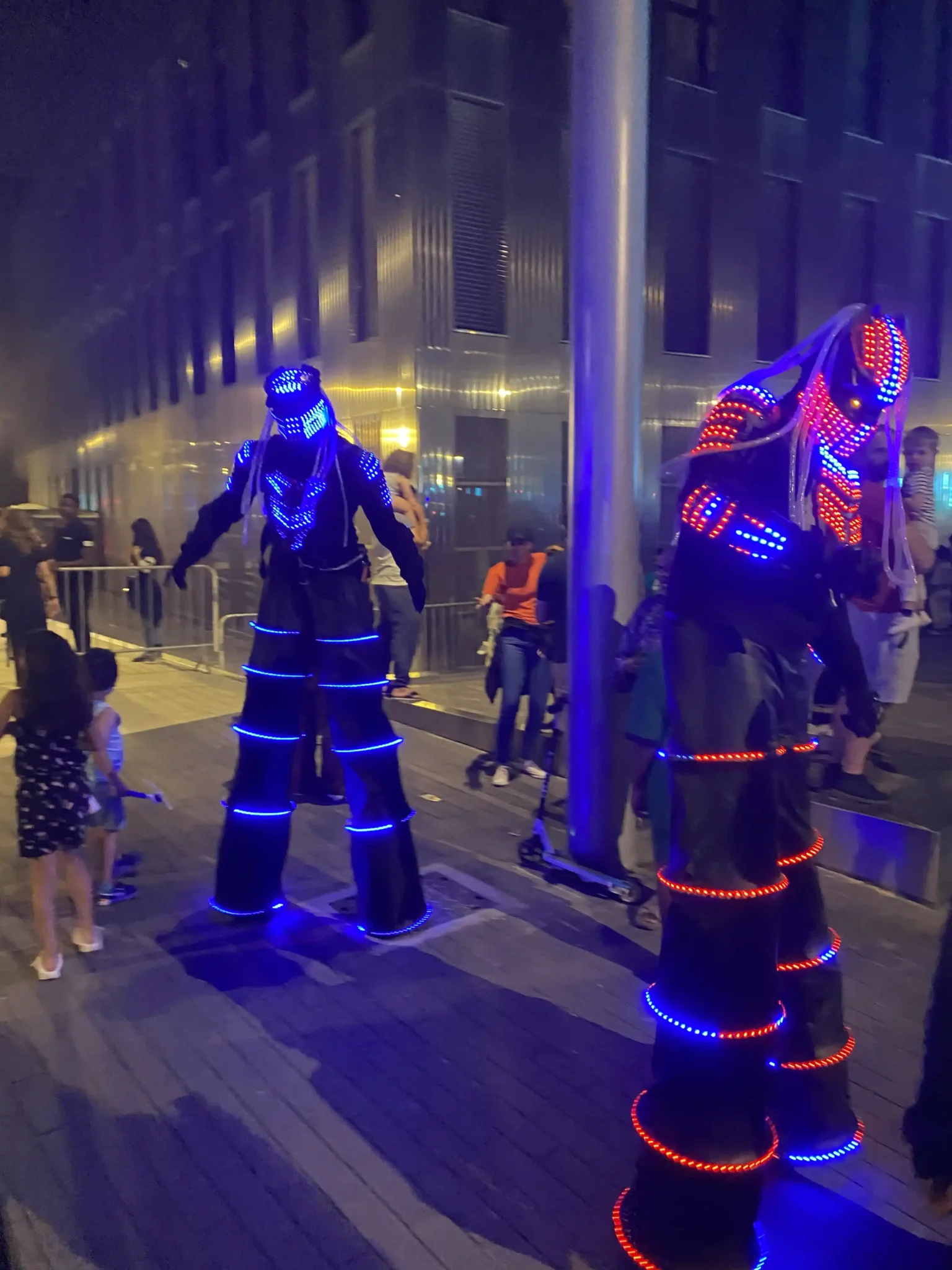 Performers sur échasses avec costumes LED lumineux lors d’un spectacle nocturne.