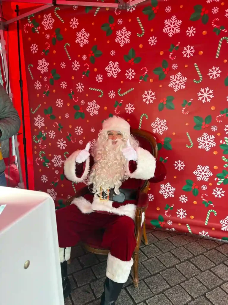 Animation de Noël avec un Père Noël accueillant le public lors d’un événement extérieur.